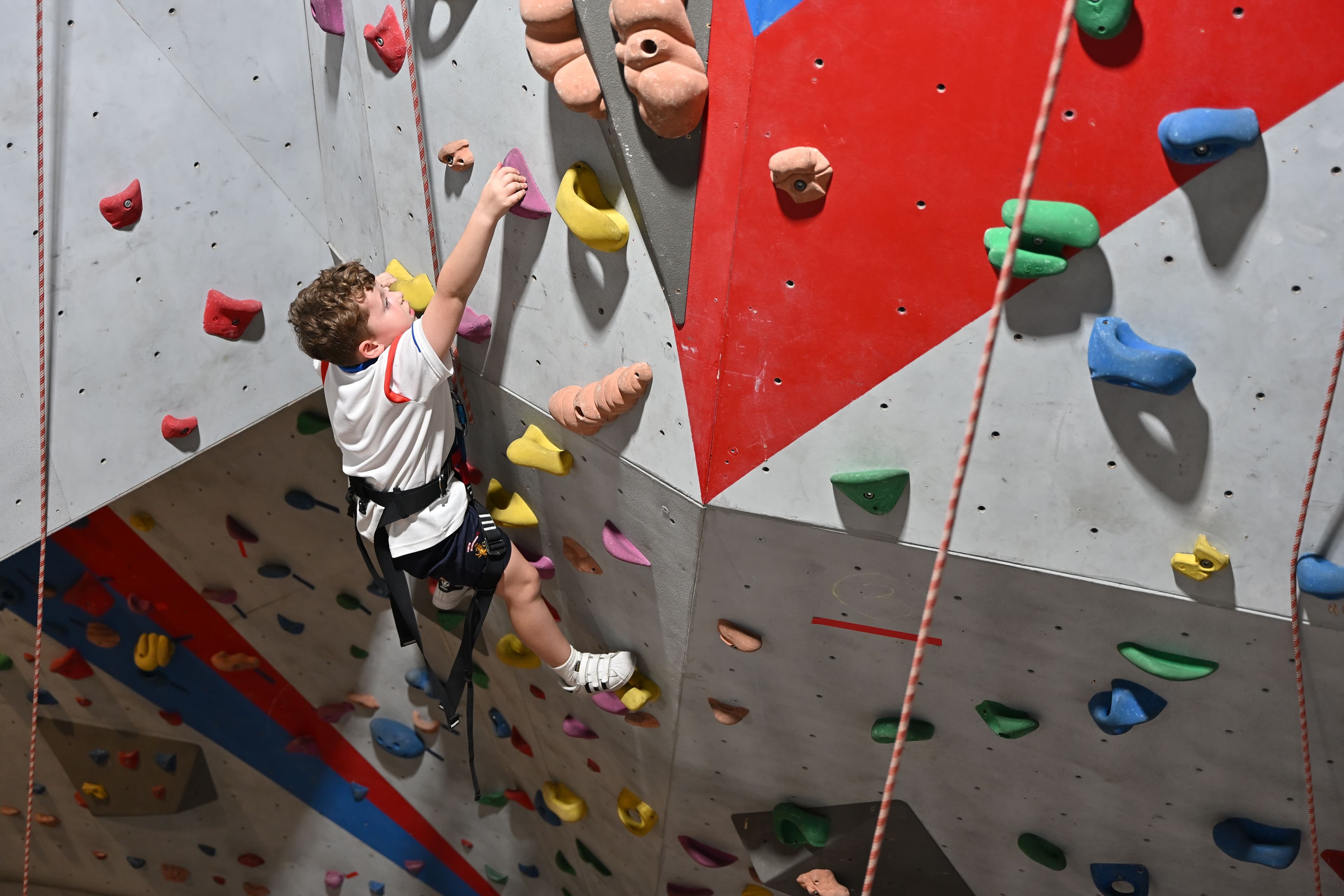 Young boy actively rock climbing indoors on a colorful wall with various holds.