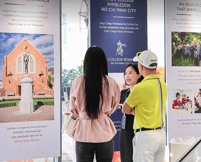 Three people converse at an exhibition booth featuring King's College Wimbledon Ho Chi Minh City displays.